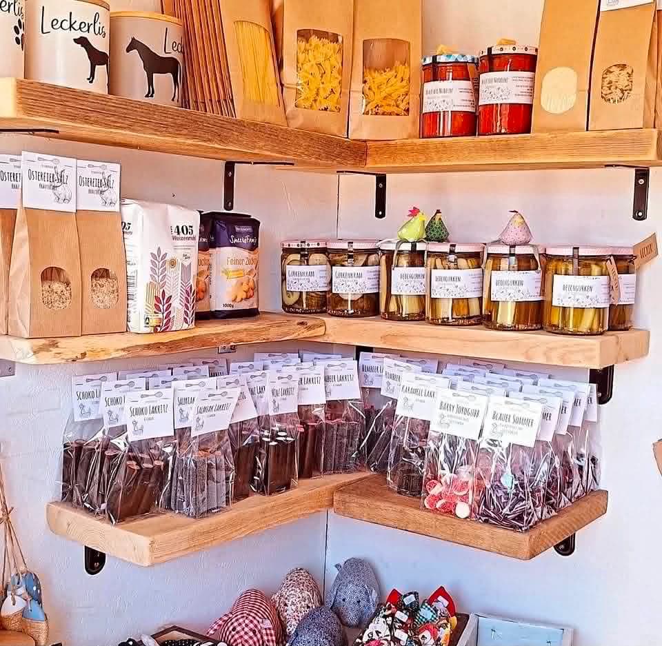 Innenansicht Verkaufshäuschen am Deich — Holzregale mit skandinavischer Lakritz (Schoko-, Salmiak-, Karamell-Lakritz, Barry Jordgubb), Eingelegtem in Gläsern (Gurken, Linsen), Mehl, Pasta und genähten Stofftieren.